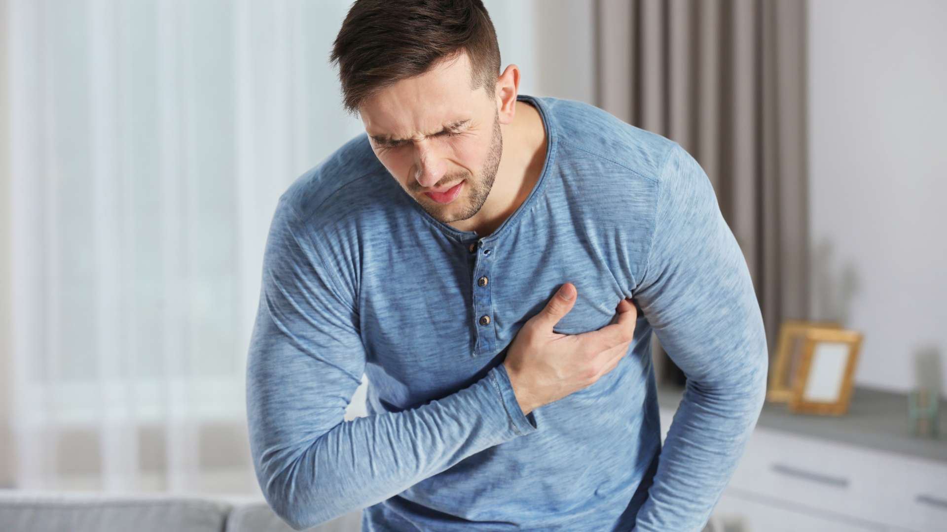 Jeune homme tee-shirt bleu manches longues qui se tient le coeur d'une main en souffrant